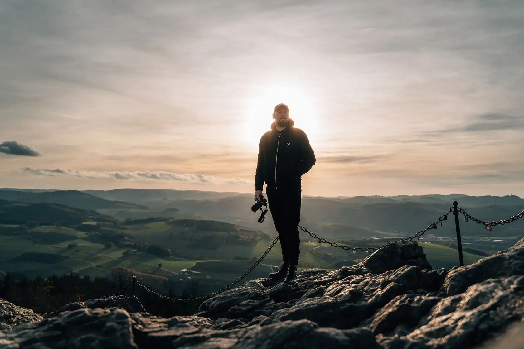 Videoproduzent mit Kamera auf Berggipfel bei Sonnenuntergang – Mocanox Outdoor-Dreh in eindrucksvoller Landschaft