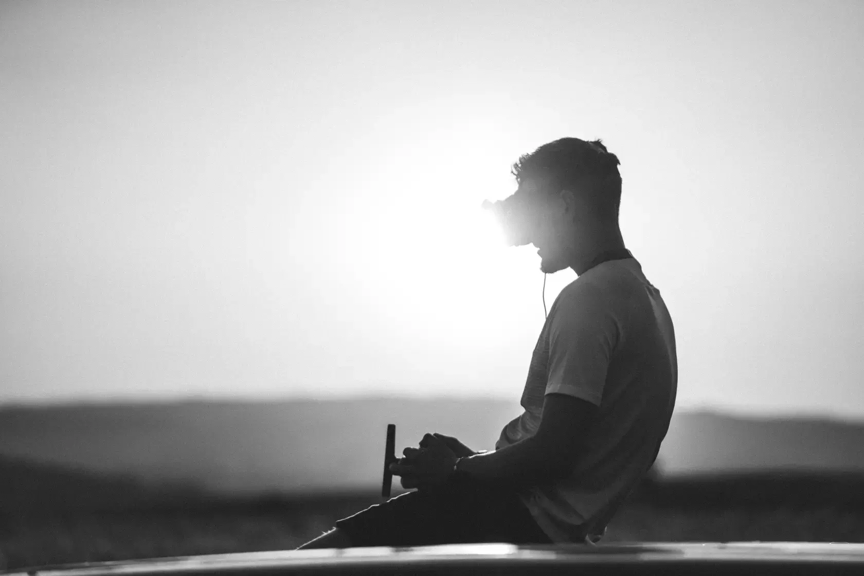 FPV Drohnenpilot sitzt auf Autodach im Sonnenuntergang bei Tourismusproduktion